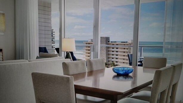 A modern dining area with a wooden table and beige upholstered chairs, overlooking a cityscape and the ocean. - Charming 3-bedroom Gulf-view villa with many amenities in amazing Marco Island (Marco Island)