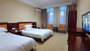 A hotel room with two beds, a television, a desk, and a window with curtains.