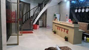 A hotel lobby with a reception desk, a staircase, and a reception area with a clock on the wall.