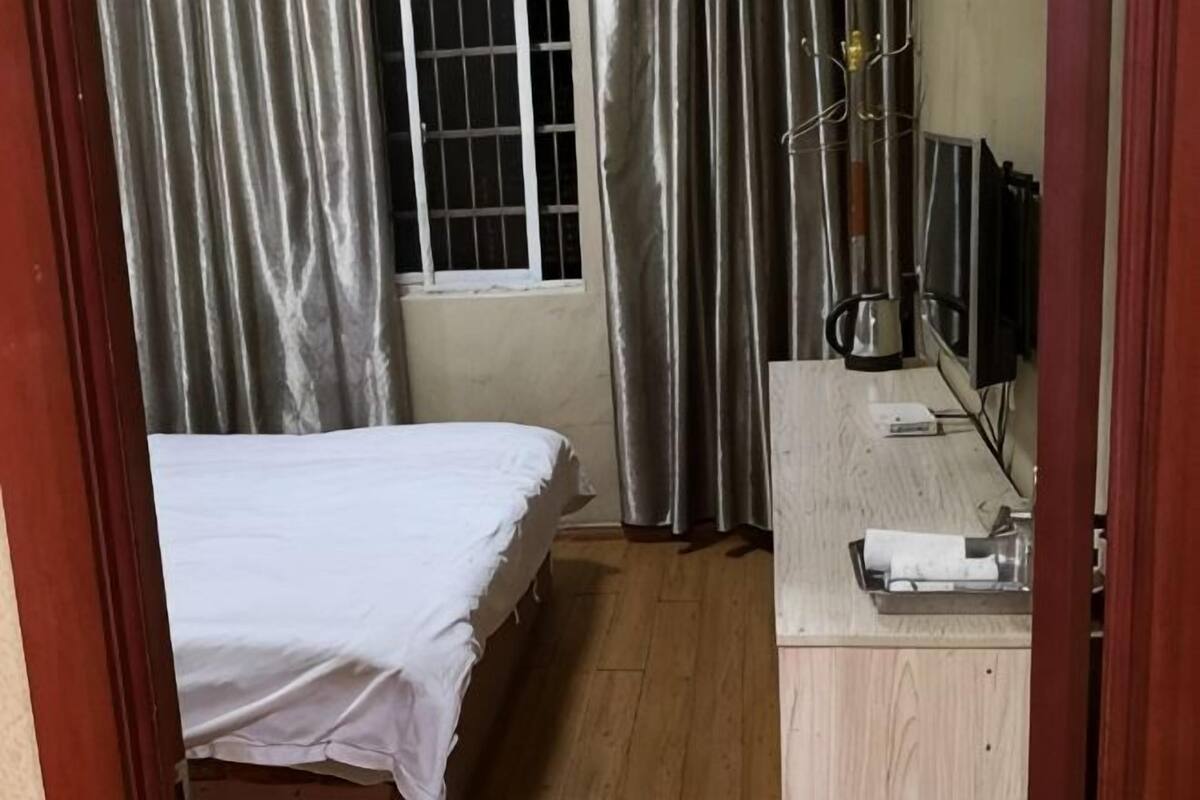 Una habitación con cama, un escritorio de madera, una ventana con cortinas y un radiador.