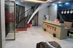 Un vestíbulo de hotel con mostrador de recepción, una escalera y un área de recepción con un reloj en la pared.
