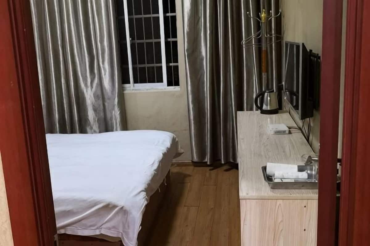 A room with a bed, a wooden desk, a window with curtains, and a radiator.