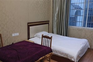 A room with two beds, a window with curtains, and a view of buildings outside.
