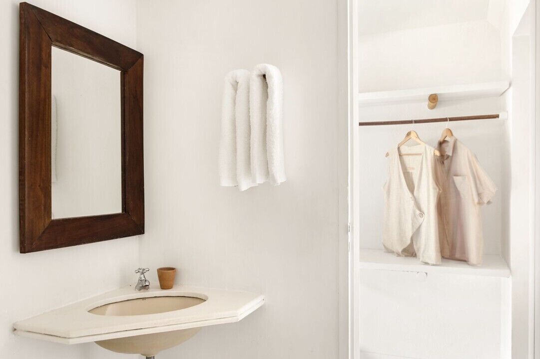 A bathroom with a wooden-framed mirror, a white sink, and two white towels hanging on the wall.