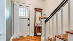 A hallway with a white door, wooden flooring, a white staircase with a black handrail, and a decorative mirror with a wooden frame. - Nestled Victorian Historic Area (Guthrie)