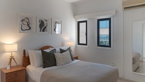 A bedroom with a large bed, two bedside tables, a nightstand, and a window with a view. - Phaedrus Living Seaview Phinikoudes Flat (Larnaca)
