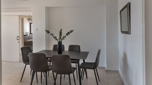 A dining area with a rectangular table, six chairs, a vase with green foliage, and a framed picture on the wall. - Phaedrus Living Seaview Phinikoudes Flat (Larnaca)