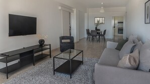 A modern living room with a flat-screen TV, a glass coffee table, a sofa, and a dining area in the background. - Phaedrus Living Seaview Phinikoudes Flat (Larnaca)
