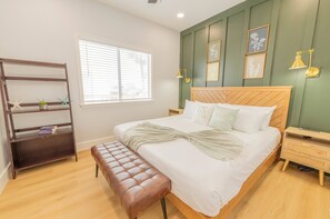 Ein ordentlich eingerichtetes Schlafzimmer mit Bett, Bank, Nachttischen und einem Bücherregal.