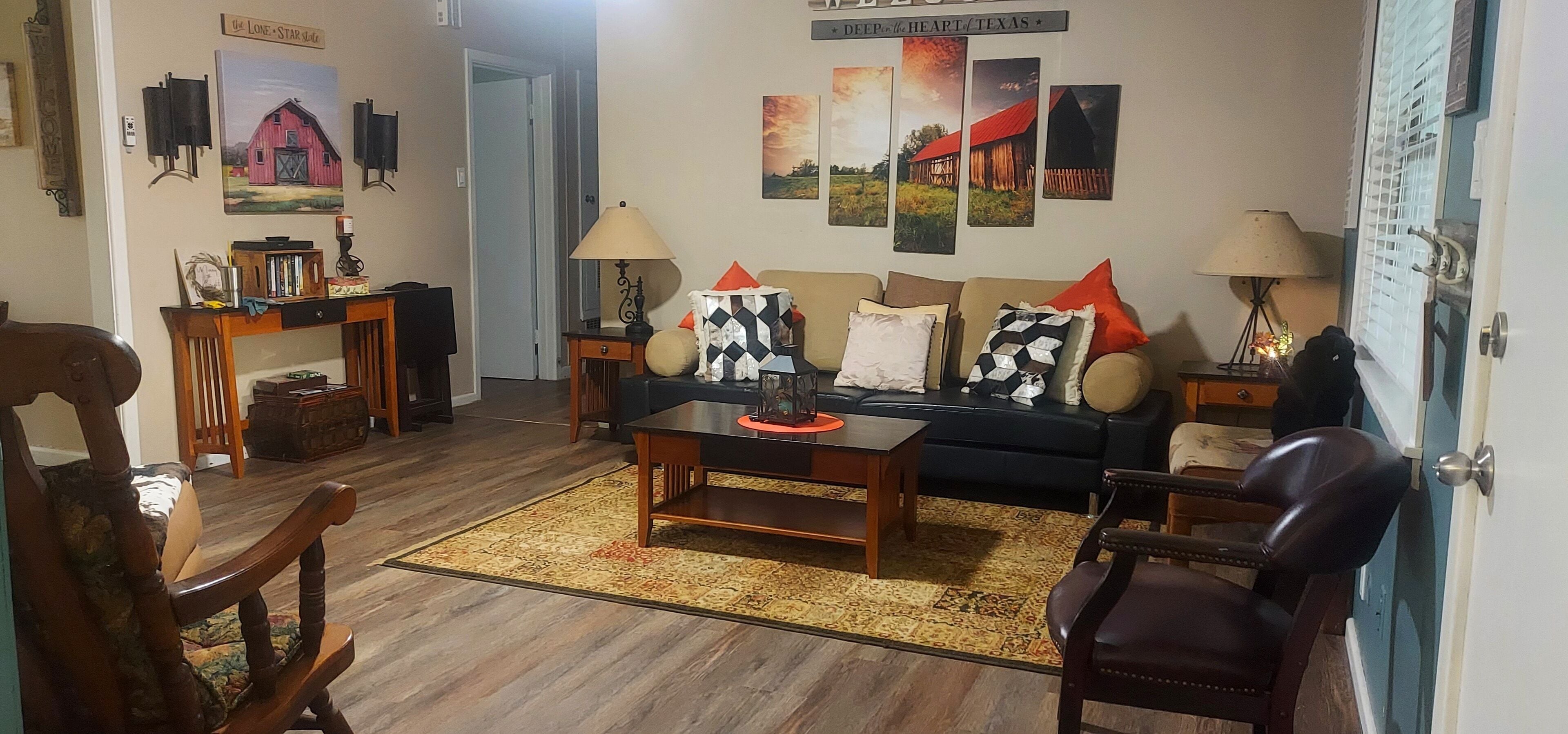 Una sala de estar acogedora con un sofá, una mesa de centro y una alfombra. Hay lámparas de pared y un cuadro de un granero.