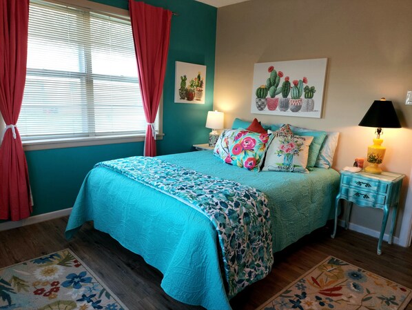 Cozy bedroom with a comfortable bed, window, and cactus artwork.