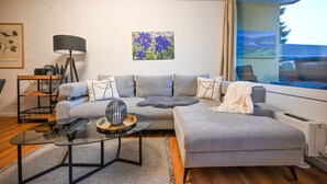 A modern living room with a grey sectional sofa, a glass coffee table, and a painting of blue flowers on the wall. - Domizil Deluxe Eleven (Kaprun)
