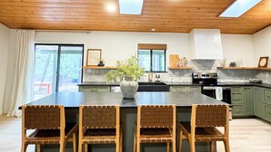 A kitchen with wooden ceiling beams, a central island with chairs, and a large window.