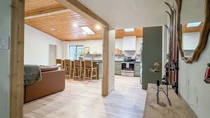A spacious living area with a wooden ceiling, a sofa, a dining table, and a kitchen in the background.