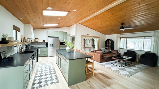 A spacious living area with a kitchen, wooden ceiling, and a large window.