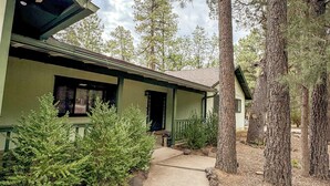 A green building with a covered porch, surrounded by trees and a concrete pathway.