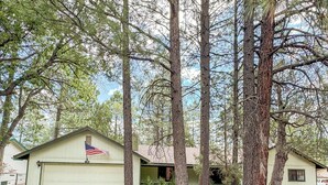 A single-story house with a garage, surrounded by tall pine trees.