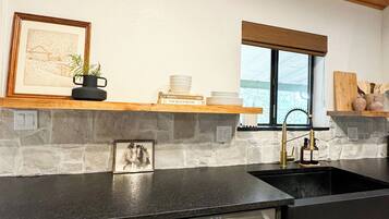 A kitchen with a stone backsplash, wooden ceiling, and a window with blinds.