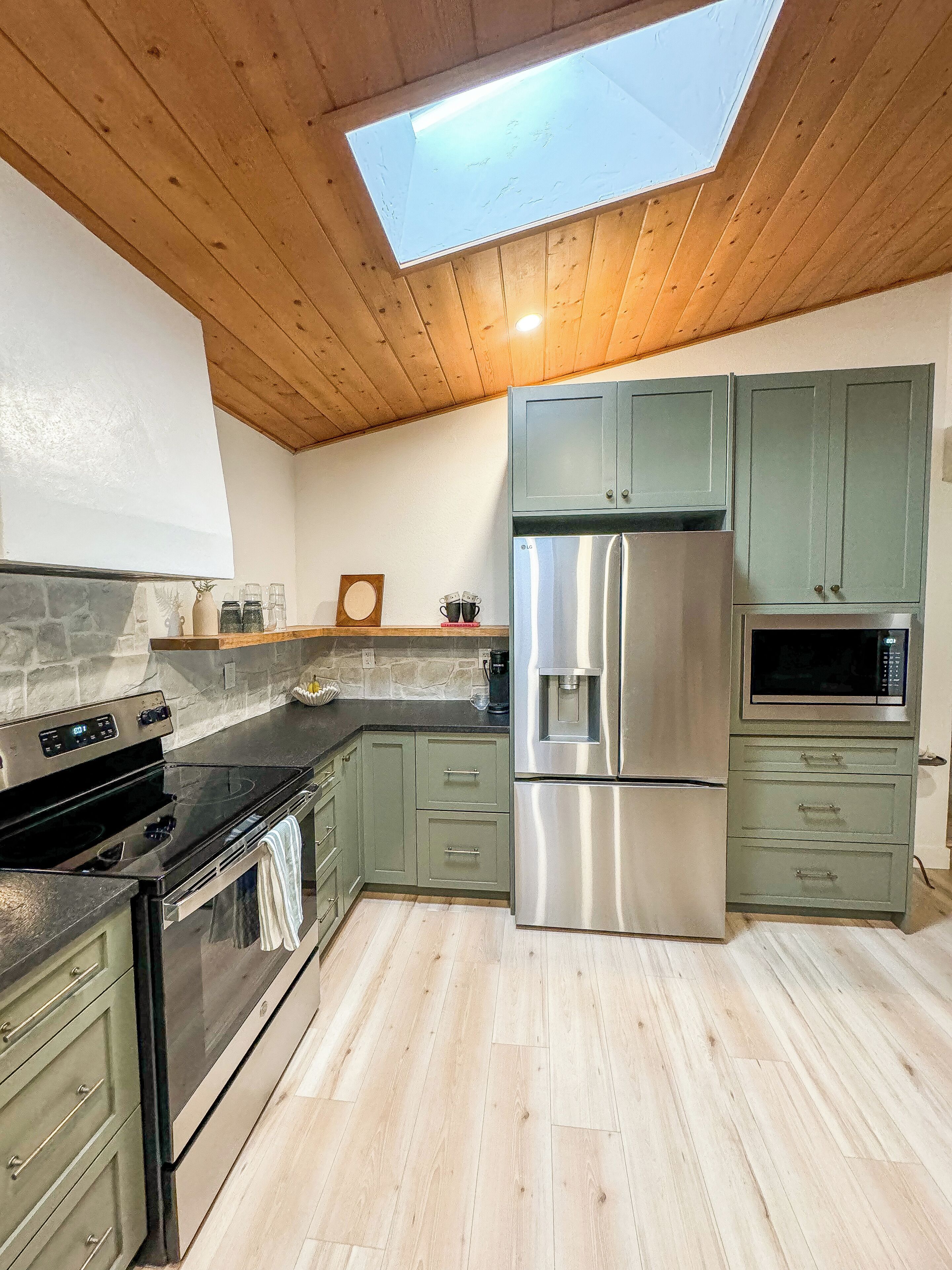A modern kitchen with a skylight, stainless steel appliances, and light green cabinets.