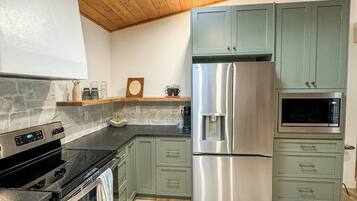 A modern kitchen with a skylight, stainless steel appliances, and light green cabinets.