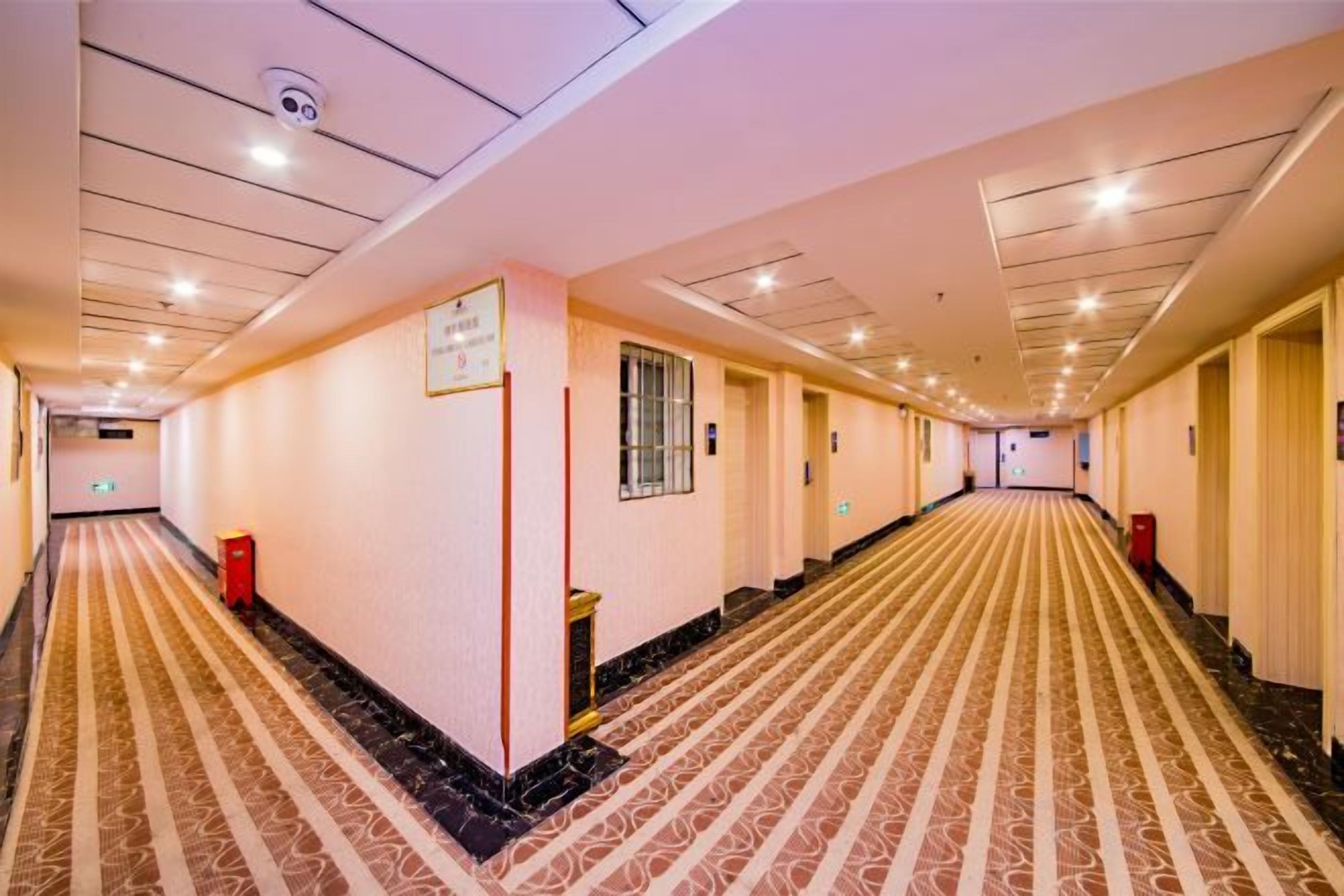 Un pasillo de hotel con alfombra estampada, puertas y un letrero en la pared.