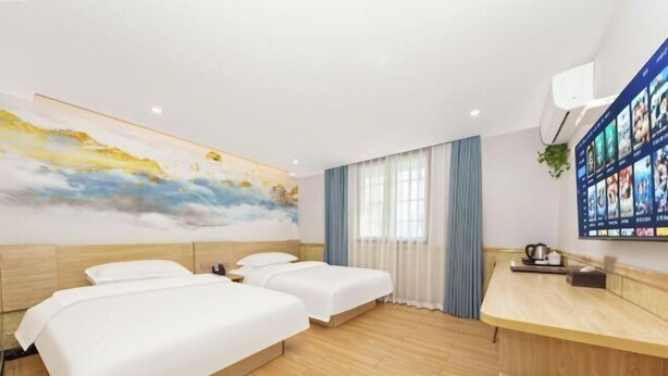 A hotel room with three beds, a wooden floor, a large painting on the wall, a TV mounted on the wall, and a desk with a plant. - Changsha Xiaoyuan Selected Hotel (Changsha)