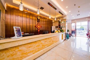 A hotel reception area with a wooden reception desk, a digital screen, and a large window offering a view of the outside. - Changsha Xiaoyuan Selected Hotel (Changsha)