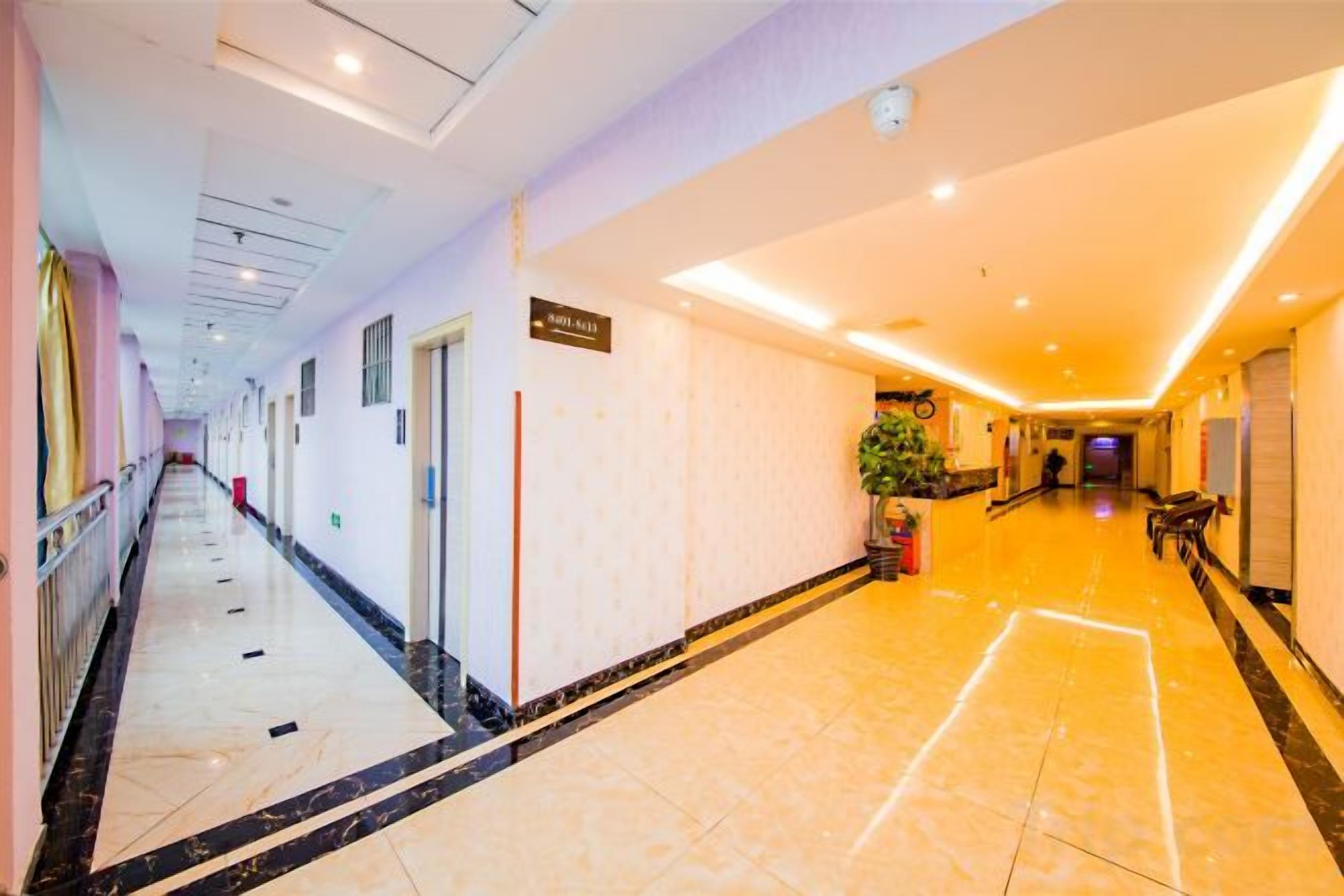 Un pasillo de hotel con suelo de mármol, puertas a la izquierda y un mostrador de recepción a la derecha.