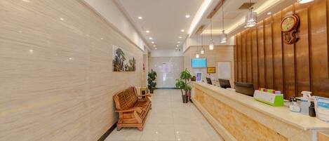 A hotel reception area with a reception desk, seating area, and a wall-mounted clock.