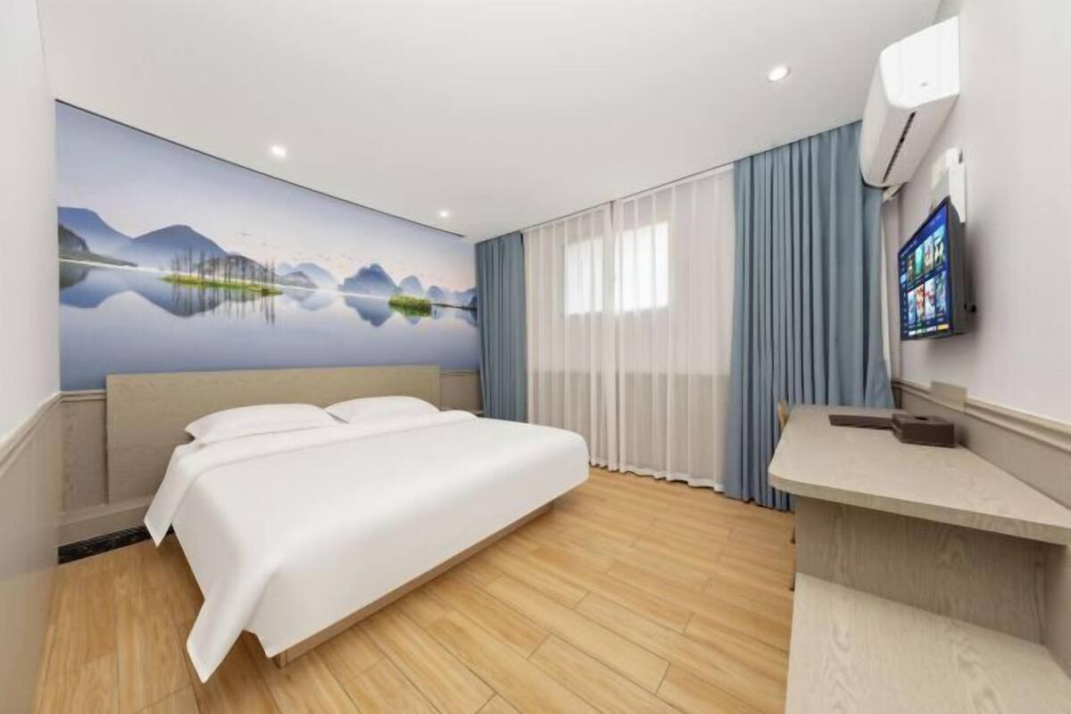 A hotel room with a bed, a TV, a painting, and a window with curtains.