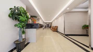 Un hall de hotel con una recepción, una planta en maceta, una zona de estar y un espejo grande en la pared.