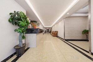 A hotel lobby with a reception desk, a potted plant, a seating area, and a large mirror on the wall. - Changsha Xiaoyuan Selected Hotel (Changsha)