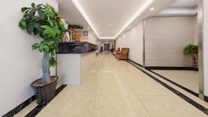 A hotel lobby with a reception desk, a large potted plant, a wooden chair, and a tiled floor. - Changsha Xiaoyuan Selected Hotel (Changsha)