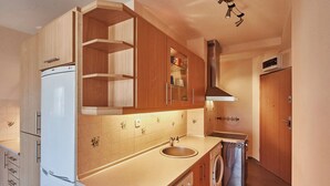 Una cocina compacta con armarios de madera, un lavamanos empotrado, una campana extractora de acero inoxidable y una lavadora y secadora pequeñas.