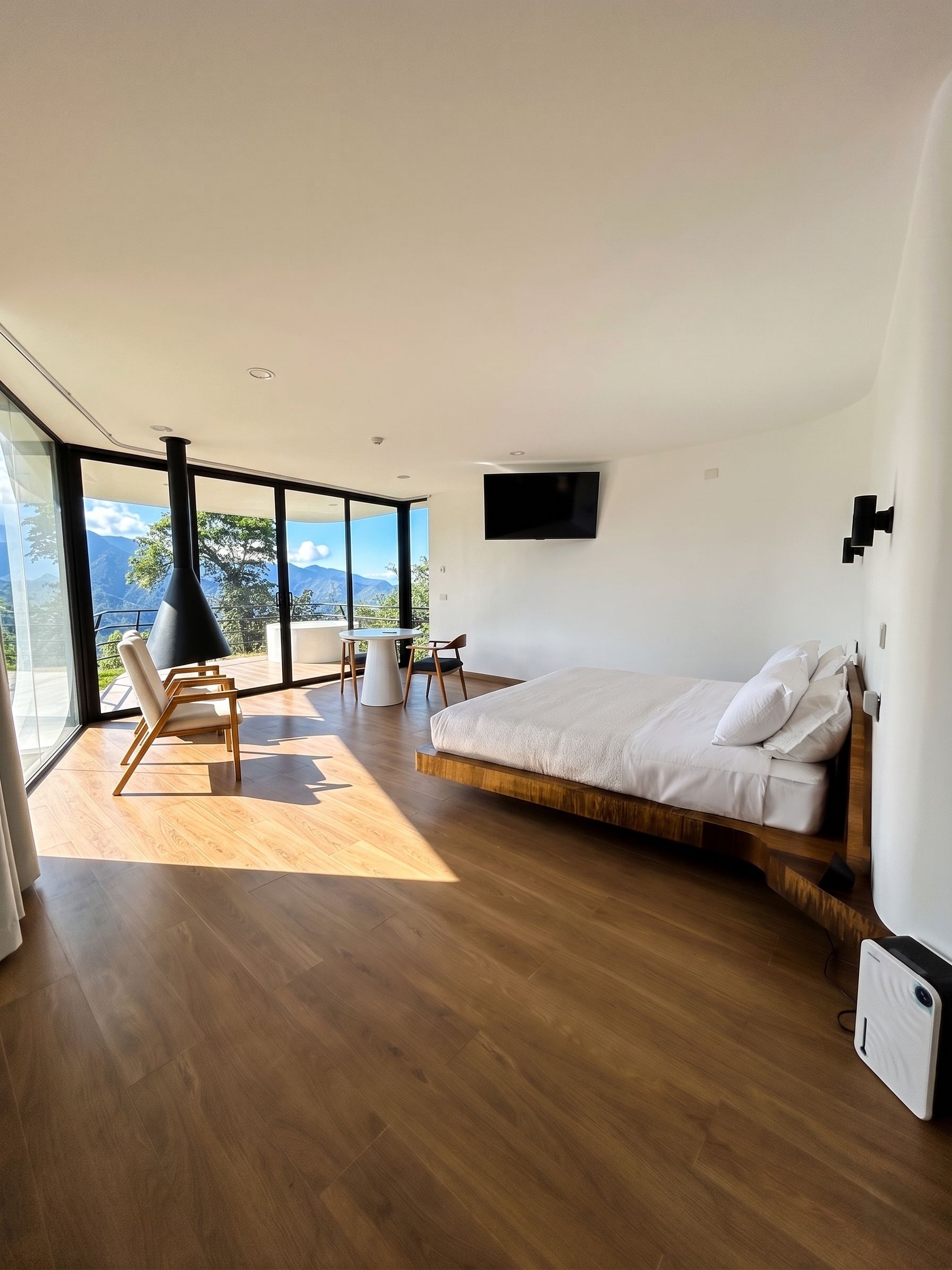 A modern bedroom with a large bed, a TV mounted on the wall, and a balcony with a view of mountains.