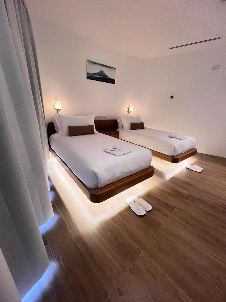 Quarto de hotel com duas camas, piso de madeira e um quadro na parede.