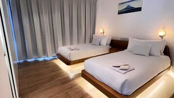 A hotel room with two beds, wooden flooring, a large window with curtains, and a painting on the wall.