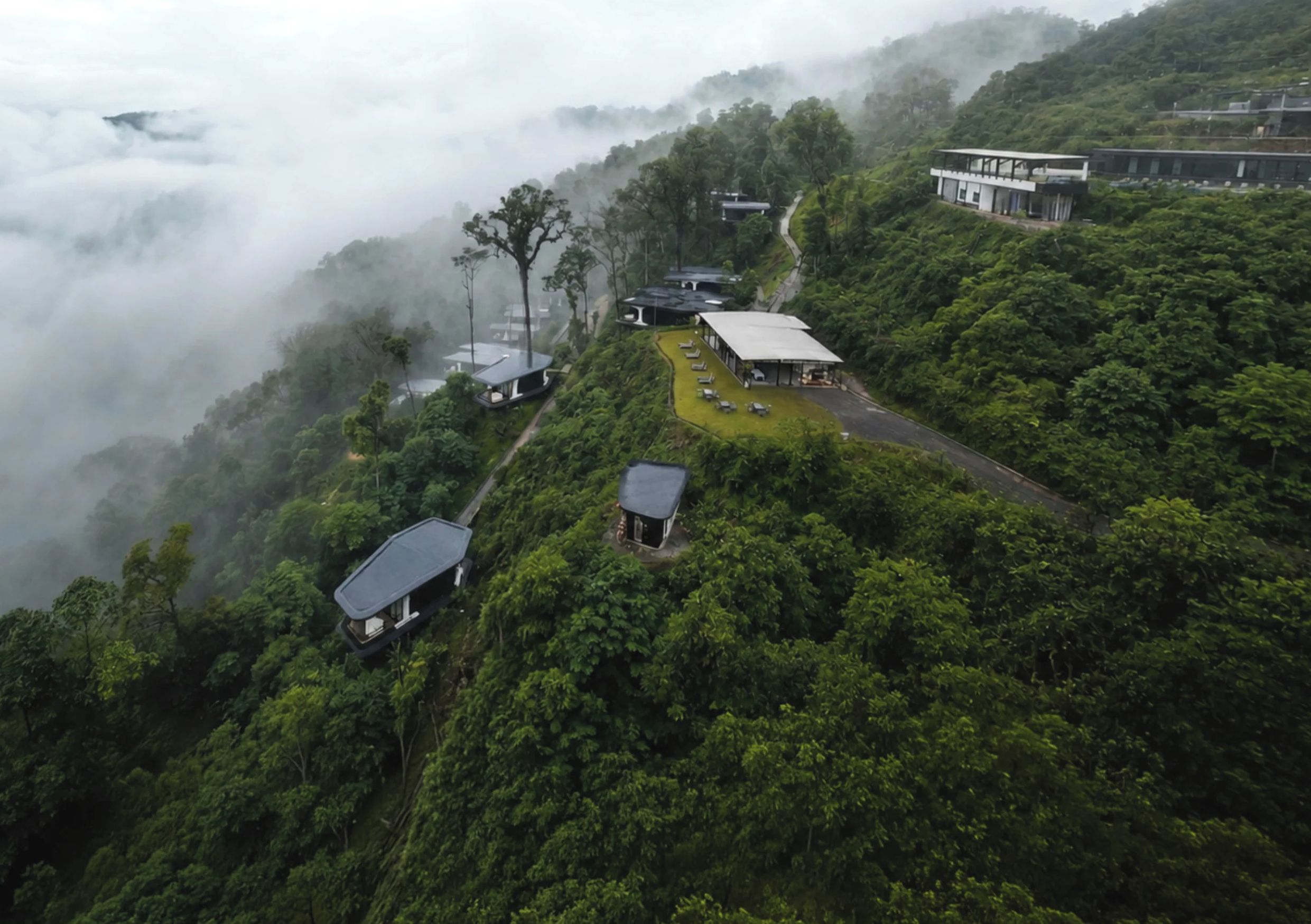 Uma região montanhosa com vários edifícios, incluindo uma construção grande com telhado plano e edifícios menores com telhados inclinados.