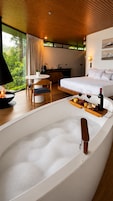 Quarto de hotel moderno com uma banheira grande, área de refeições e uma cama.