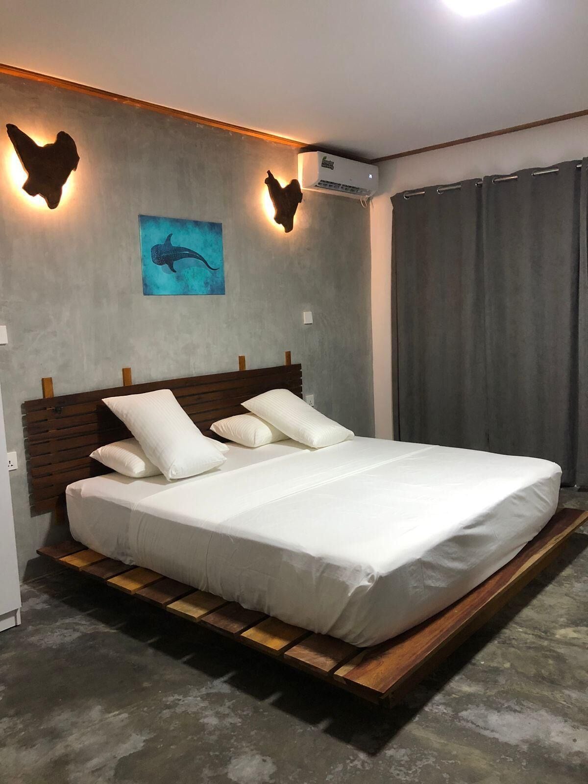 A modern bedroom with a wooden platform bed, a wall-mounted air conditioner, and a dolphin-themed artwork.