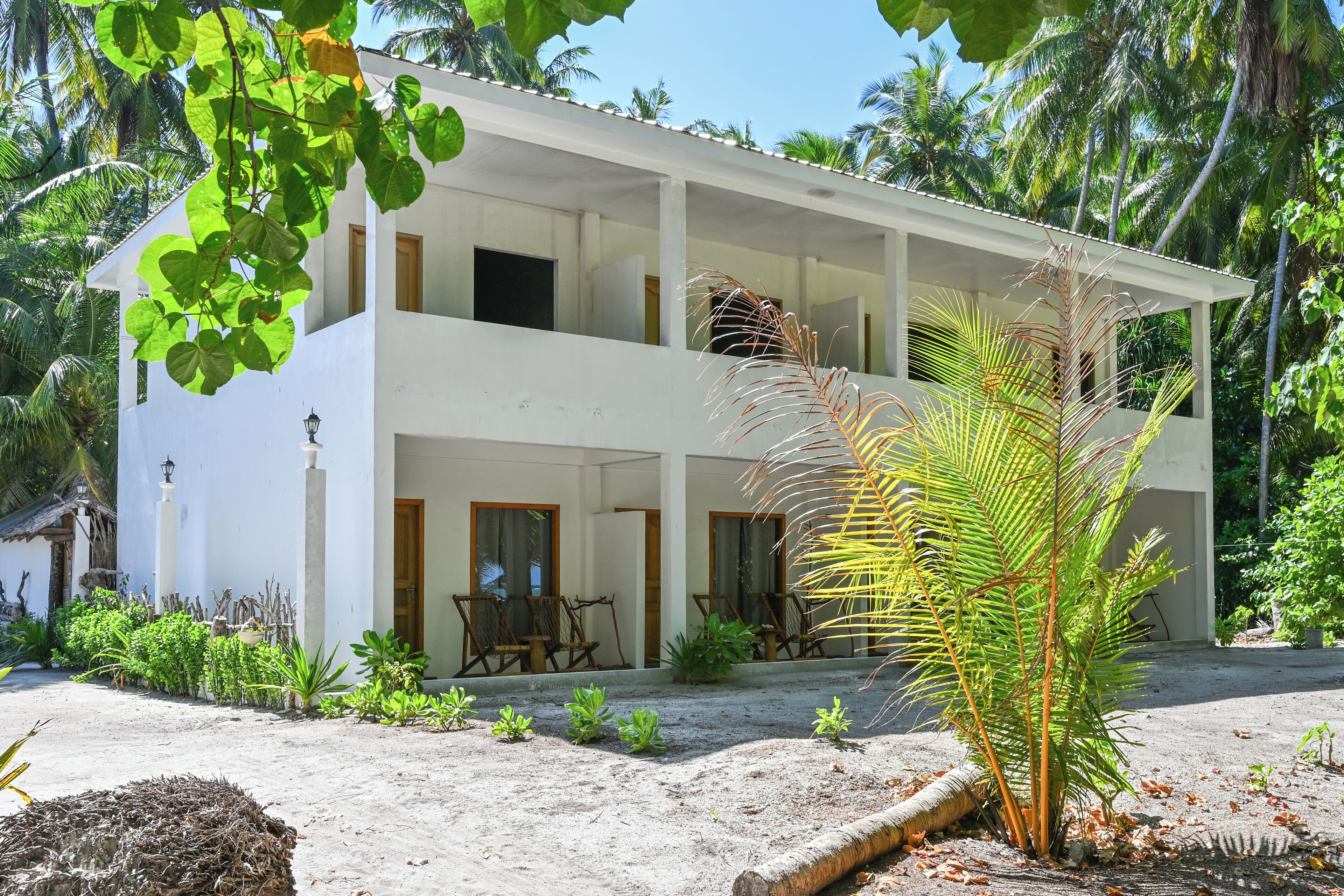 Un bâtiment à deux étages doté d’un balcon, entouré d’une végétation tropicale.
