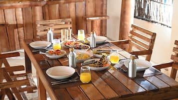 Una mesa de comedor de madera dispuesta con platos, cubiertos y bebidas, rodeada de sillas de madera.