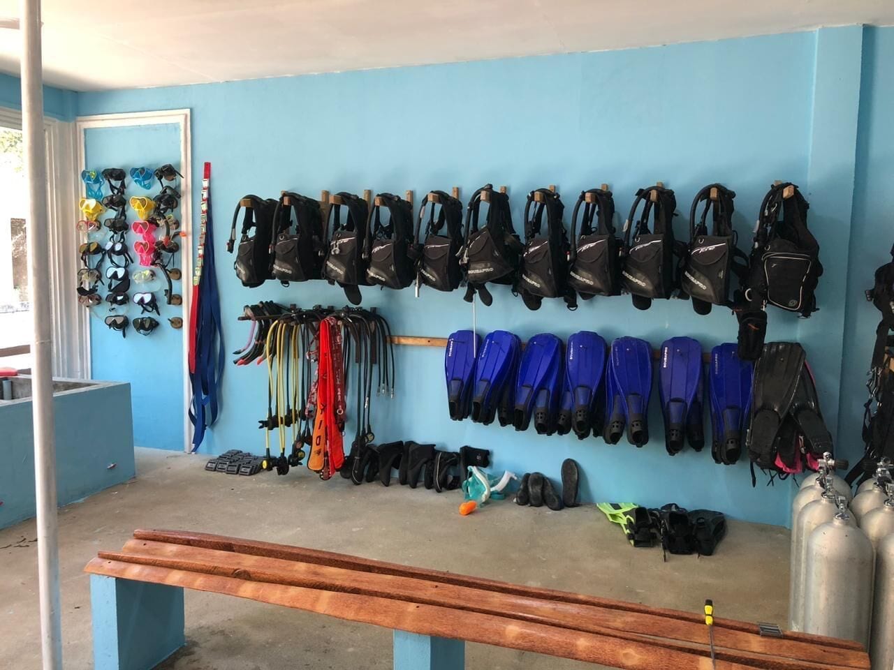 Ein Zimmer mit blauer Wand, das verschiedene Tauchausrüstung wie Flossen und Schnorchel, eine Bank sowie einige verstreute Gegenstände zeigt.