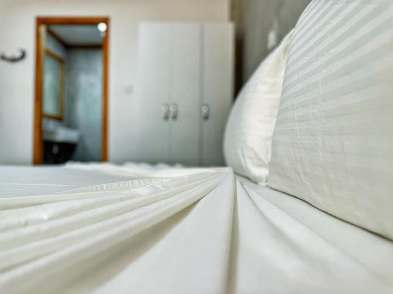 Una cama con sábanas blancas y una puerta de madera al fondo.