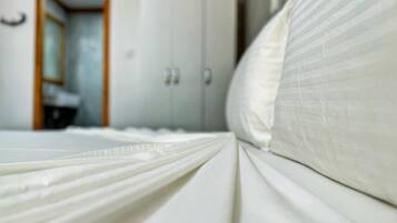 Una cama con sábanas blancas y una puerta de madera al fondo.