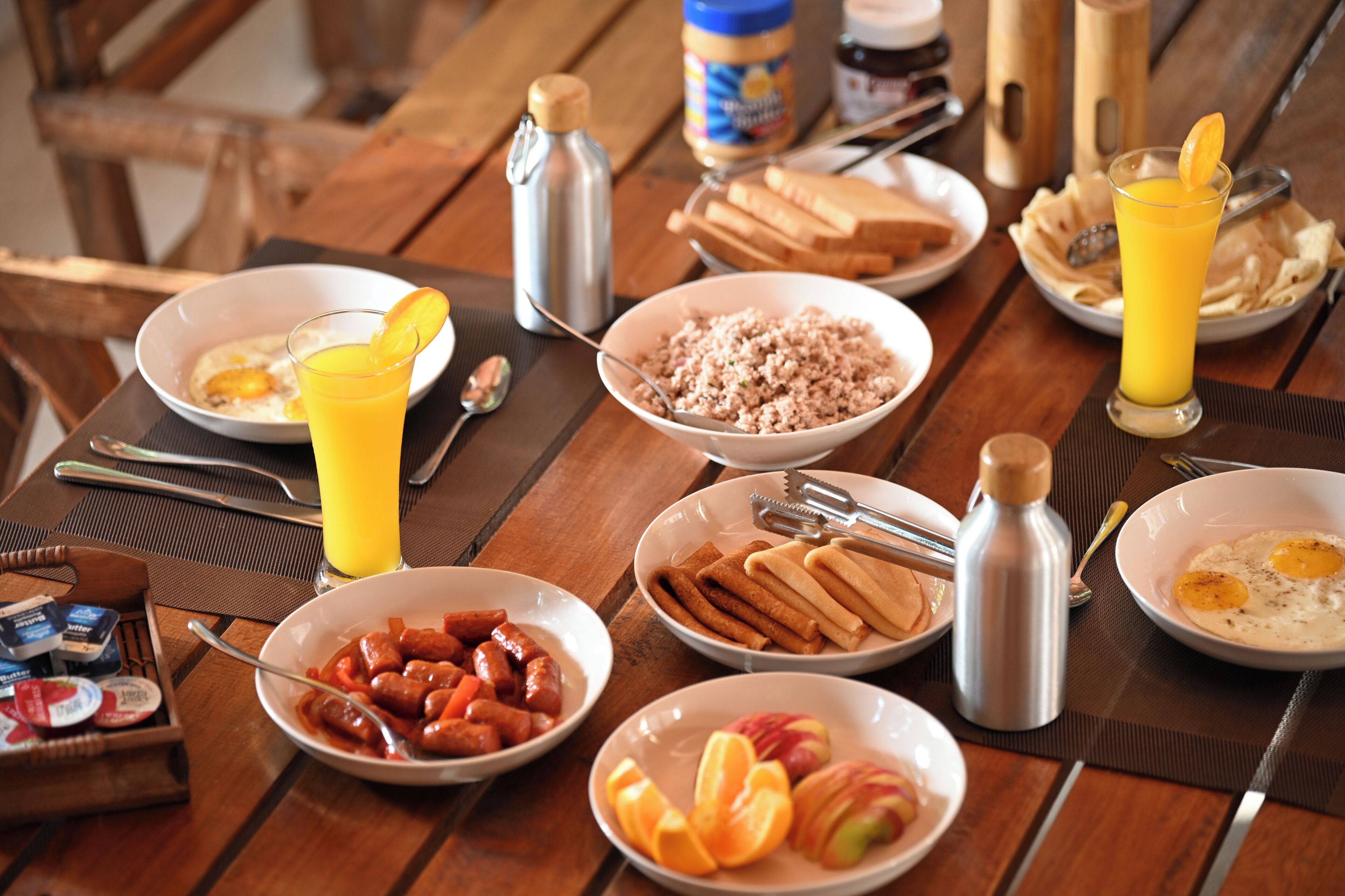 A breakfast table with various food items, utensils, and a thermos.
