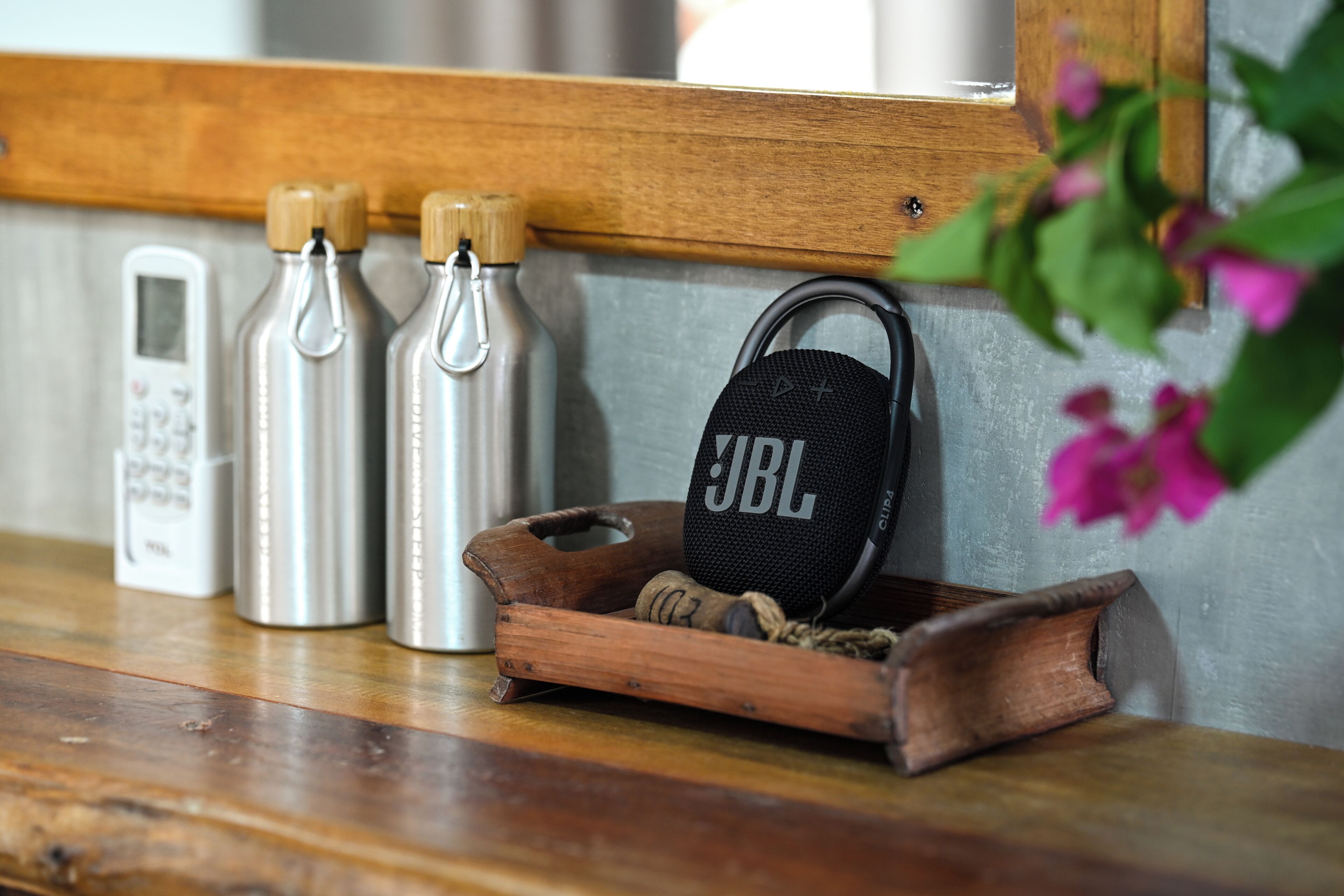Un estante de madera con tres botellas de agua de acero inoxidable, un altavoz JBL y una pequeña bandeja de madera con cuerda.