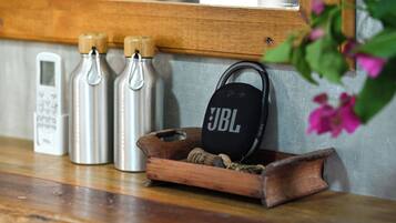 Un estante de madera con tres botellas de agua de acero inoxidable, un altavoz JBL y una pequeña bandeja de madera con cuerda.