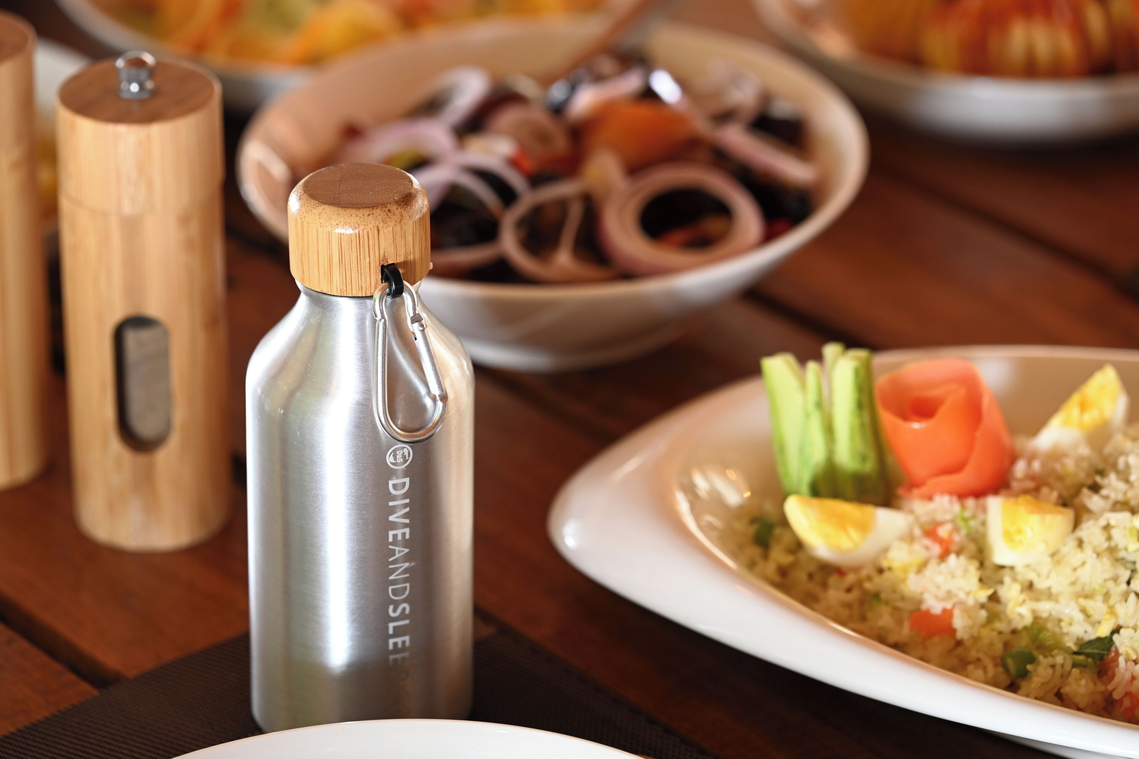 A table with a stainless steel water bottle, a wooden pepper mill, and a plate of food.