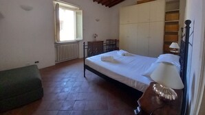 A bedroom with a bed, a radiator, a window, a wooden wardrobe, and a green bench.